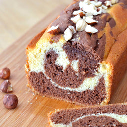 Un cake marbrAC avec des tourbillons de chocolat et une garniture de noisettes est posAC sur une planche A? dACcouper en bois.