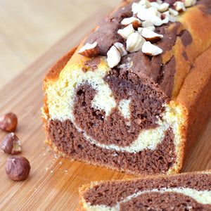 Un cake marbrAC avec des tourbillons de chocolat et une garniture de noisettes est posAC sur une planche A? dACcouper en bois.