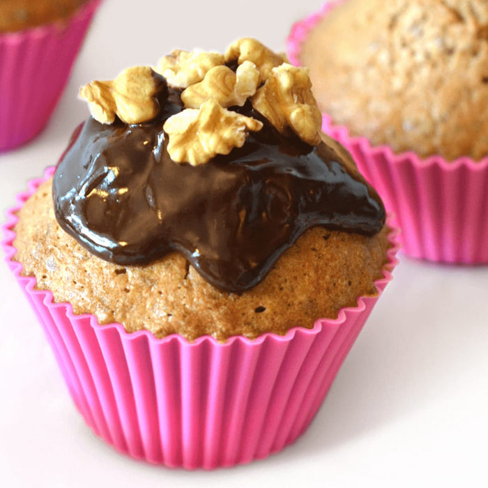 Un dAClicieux muffin avec un glaA?age au chocolat et une garniture aux noix dans un moule en silicone rose vif.