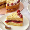 Une part de Victoria sponge cake garnie de confiture de framboises et de crème, surmontée de framboises et d'amandes effilées.
