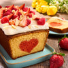Un cake avec un cA?ur rouge au centre, garni de glaA?age blanc, de fraises, de framboises et d'amandes effilACes, est posAC sur une assiette bleue avec une fraise A? cA?tAC.