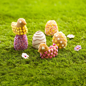 Une collection de bonbons dACcorACs en forme d'A?ufs de PAcques et de friandises en forme de poussins sont prACsentACs sur un lit de mousse verte.