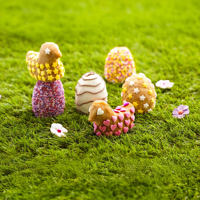 Une collection de bonbons dACcorACs en forme d'A?ufs de PAcques et de friandises en forme de poussins sont prACsentACs sur un lit de mousse verte.