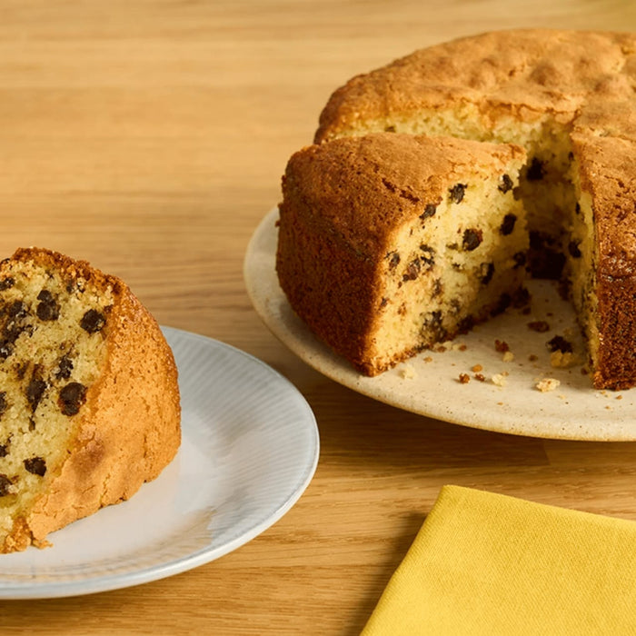 Un délicieux gâteau aux pépites de chocolat est présenté, avec une tranche déjà coupée et servie dans une assiette séparée.