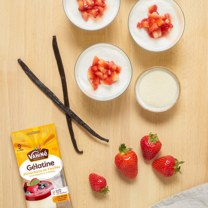 Une vue de dessus des ingrACdients du dessert A? la gAClatine Dr. Oetker et des portions prACparACes avec des fraises et des gousses de vanille sur une surface en bois.
