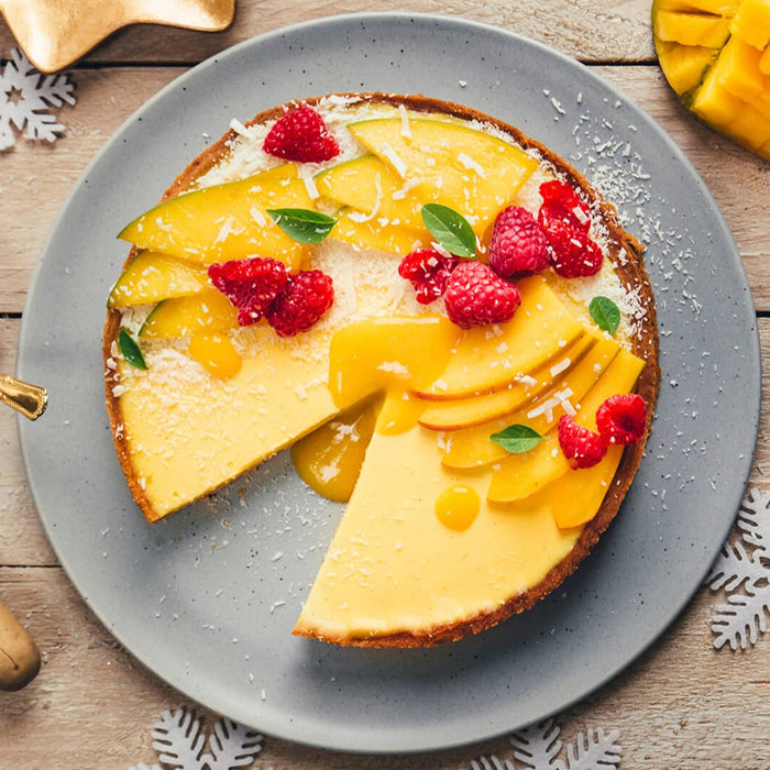 Une dAClicieuse tarte A? la mangue est prACsentACe sur une assiette, garnie de framboises et de feuilles de menthe.