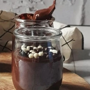 Deux pots de pudding au chocolat sont prACsentACs, l'un garni de perles de chocolat et de chocolat blanc, et l'autre avec une cuillA?re de pudding en cours d'ajout.