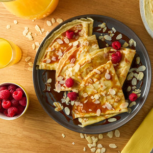 Une assiette de crAapes garnies de sauce caramel, d'amandes et de framboises, servies avec du jus d'orange.