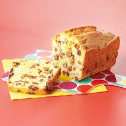 Un pain aux raisins est posé à côté d'une tranche sur une serviette à pois colorée, mettant en valeur sa texture et ses ingrédients.