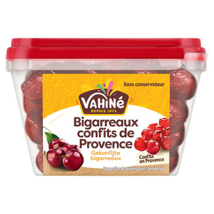 Un contenant en plastique transparent de Bigarreaux confits de Provence de la marque Vahine, aussi appelées cerises confites, est présenté avec un couvercle rouge et une étiquette montrant des cerises fraîches et confites.