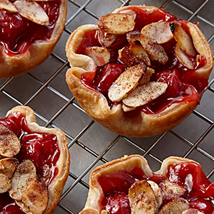 Un gros plan de mini-tartes aux cerises garnies d'amandes grillées sur une grille, présentant une délicieuse option de dessert.