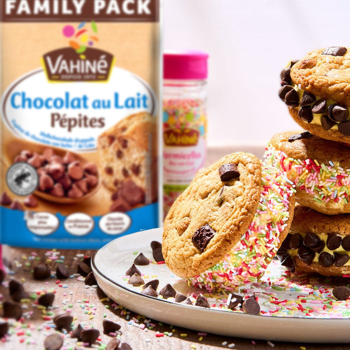 Un paquet de pépites de chocolat au lait Vahiné est présenté à côté de sandwichs glacés aux biscuits aux pépites de chocolat faits maison et recouverts de vermicelles.