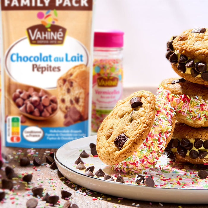 Un paquet de pépites de chocolat au lait Vahiné est présenté à côté de sandwichs glacés aux biscuits aux pépites de chocolat faits maison et recouverts de vermicelles.