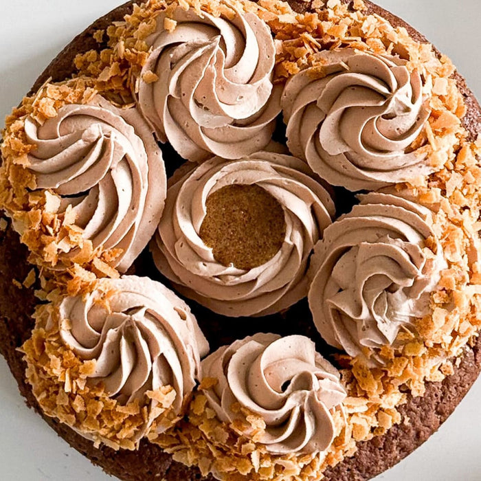 Un gâteau au chocolat décadent est décoré de tourbillons de glaçage au chocolat et de flocons de noix de coco grillés.