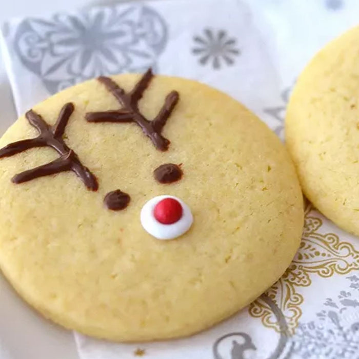 Un biscuit festif en forme de renne, dACcorAC de bois en chocolat et d'un nez rouge, repose sur une serviette dACcorative.