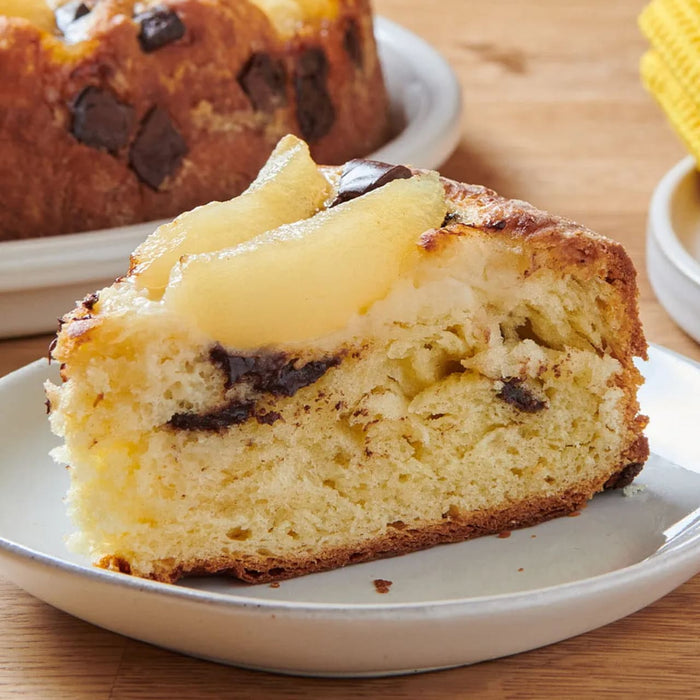 Une tranche de gActeau aux poires et aux pACpites de chocolat est prACsentACe sur une assiette, mettant en valeur sa texture moelleuse et ses dAClicieuses garnitures.