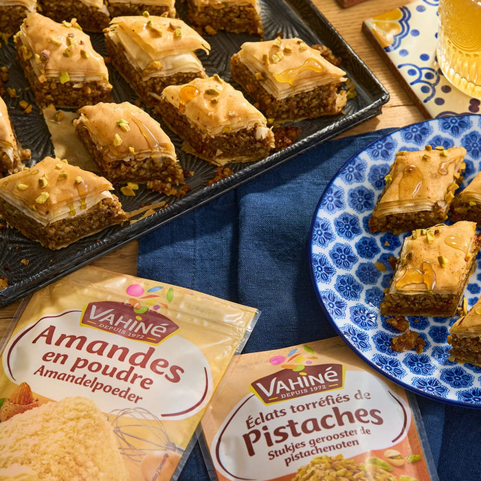 Un plateau et une assiette de baklava sont prACsentACs avec des poudres d'amandes et de pistaches de la marque VahinAC, suggACrant des ingrACdients pour le dessert.