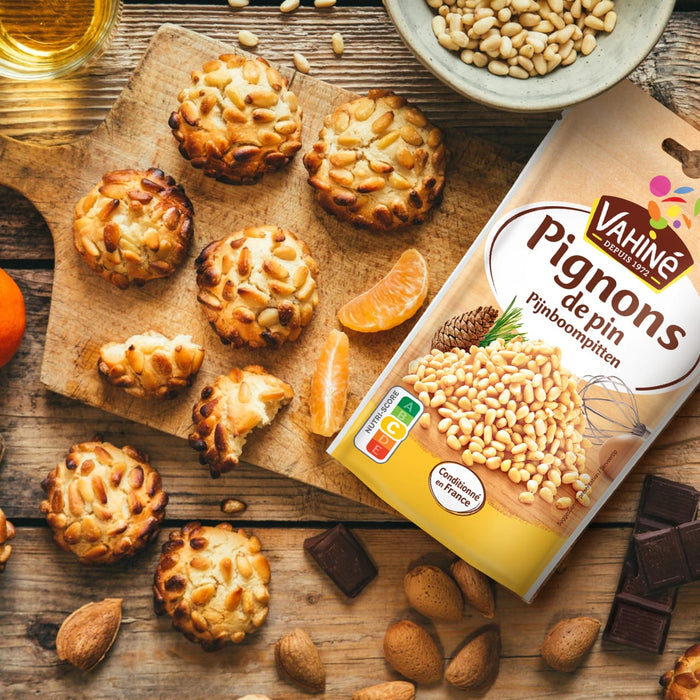 Une table en bois prACsente des panellets, des gActeaux catalans traditionnels aux amandes recouverts de pignons de pin, A? cA?tAC d'un paquet de pignons de pin VahinAC Pignons de Pins, d'amandes, de chocolat et de tranches d'orange.