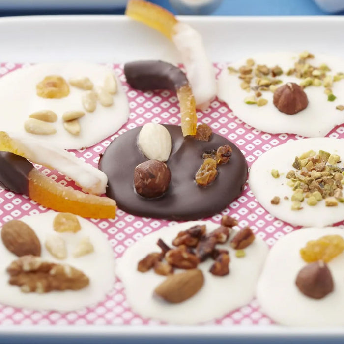 Une sAClection de mendiants au chocolat colorACs, chacun garni de divers fruits secs et confits, prACsentACs sur une surface A? motifs.