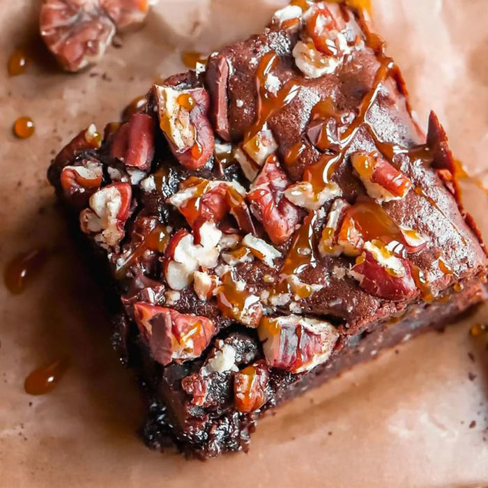 Un brownie décadent garni de noix de pécan et de sauce caramel sur du papier sulfurisé brun.