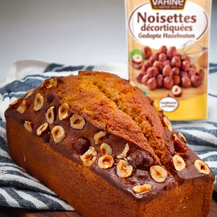 Un cake aux noisettes décoré de noisettes, à côté d'une boîte de noisettes Noisettes décortiquées.