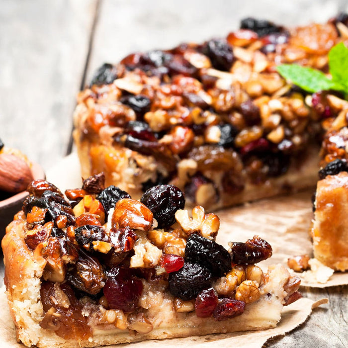 Un délicieux gâteau garni de noix et de fruits secs est présenté sur une surface en bois, avec une tranche coupée.