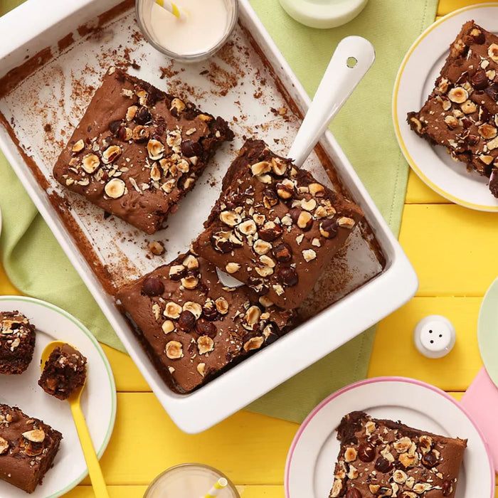 Un plateau de brownies fraîchement cuits, garnis de noix, est entouré d'assiettes contenant des portions individuelles, créant une scène de dessert chaleureuse et invitante.
