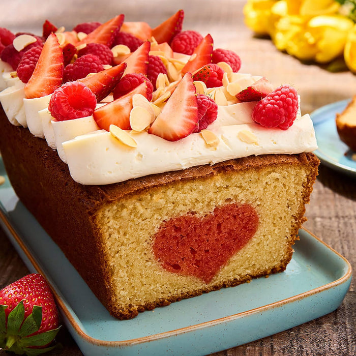 Un cake en forme de pain avec un cA?ur au centre, garni de glaA?age et de fraises et framboises fraARches.