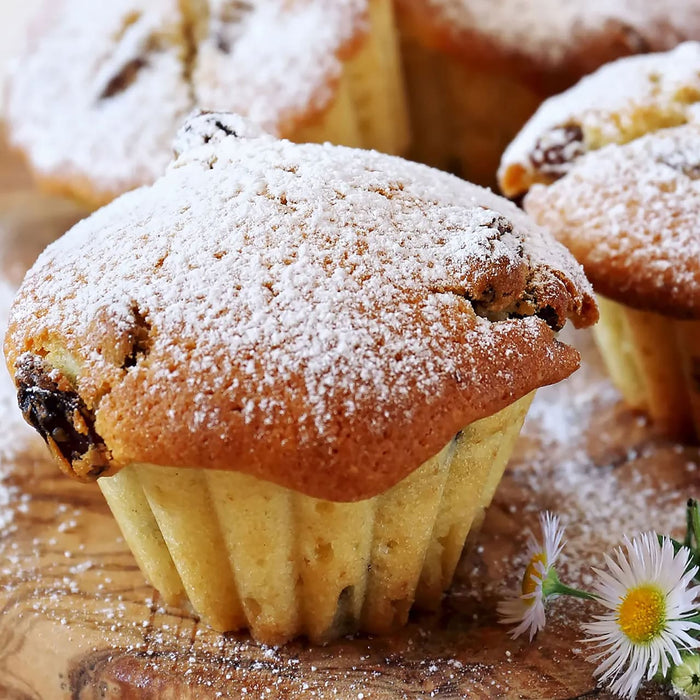 Un muffin avec une croûte dorée et une garniture de sucre en poudre est posé sur une surface en bois.