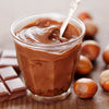 Un pot en verre rempli de pActe A? tartiner chocolat-noisette faite maison, entourAC de noisettes et de carrACs de chocolat, prACsentant une gourmandise dAClicieuse et indulgente.