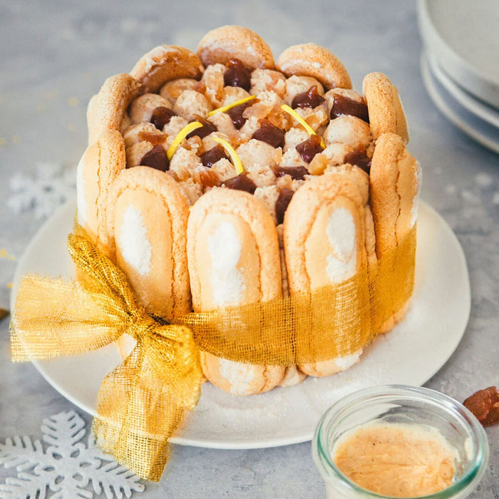 Un gActeau Charlotte magnifiquement dACcorAC avec des biscuits A? la cuillA?re et un ruban dorAC, parfait pour une occasion festive.