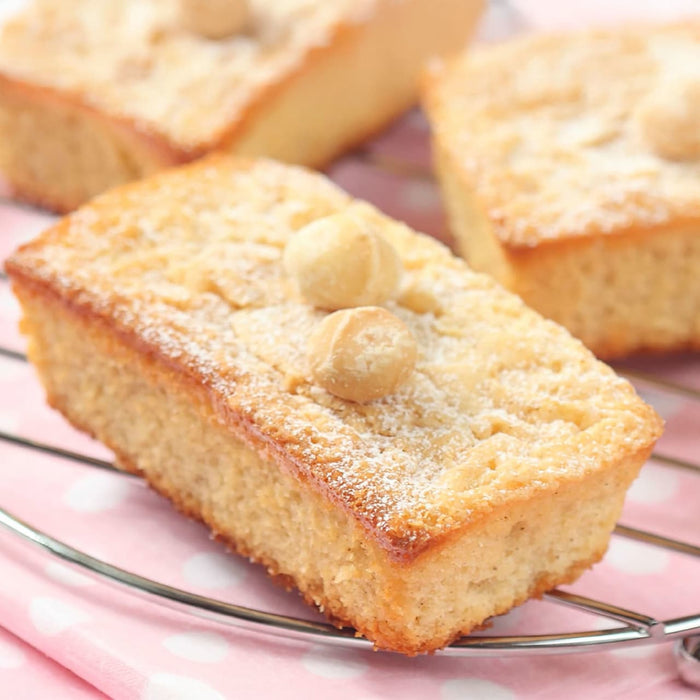 Un gros plan de blondies rectangulaires garnis de noix de macadamia et de sucre glace, prACsentACs sur une grille.
