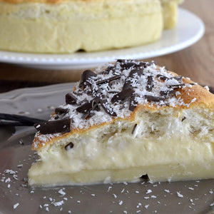 Une part de gâteau crémeux garnie de copeaux de chocolat et de noix de coco râpée repose sur une assiette grise.