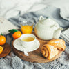 Une scA?ne de petit-dACjeuner chaleureuse avec du thAC, du jus d'orange et des viennoiseries disposACs sur un plateau en bois sur un lit, suggACrant une matinACe relaxante.