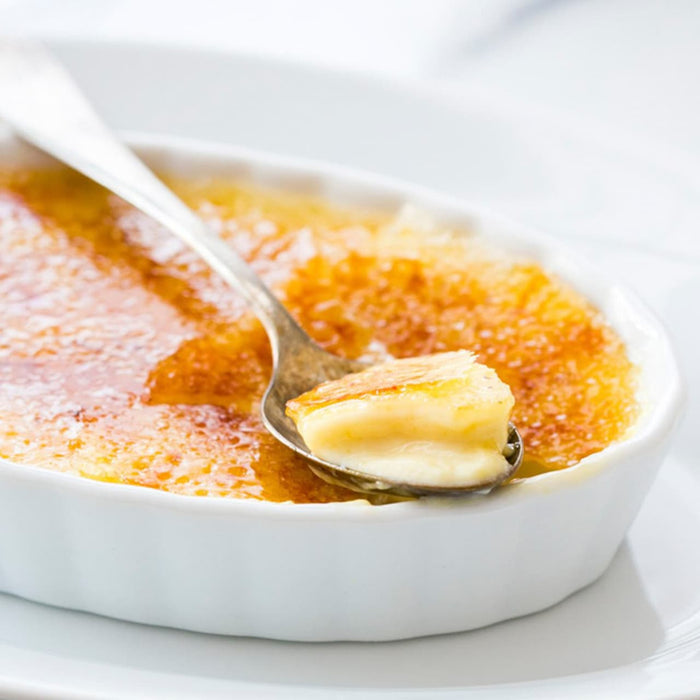 Une cuillère de crème brûlée onctueuse est soulevée d'un ramequin blanc, mettant en valeur sa croûte de sucre caramélisé.