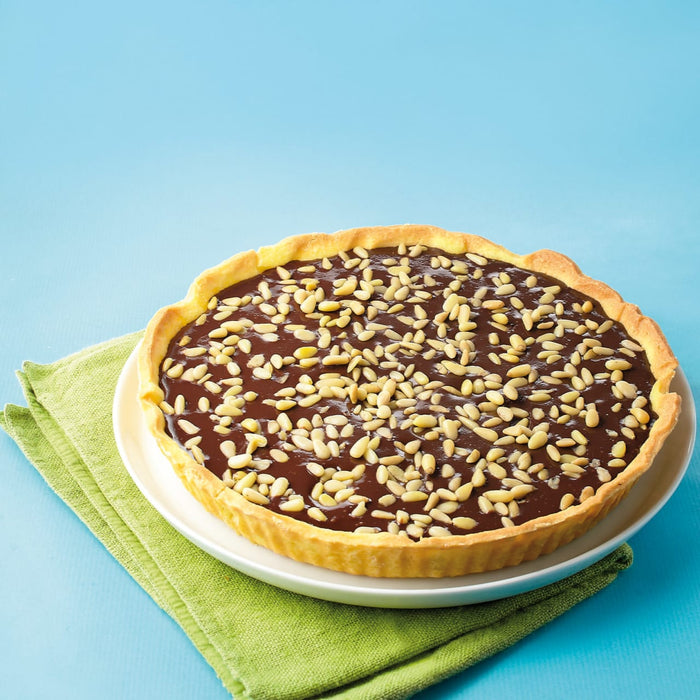 Une dAClicieuse tarte au chocolat avec une garniture de noix sur une assiette blanche, sur un fond bleu vif.