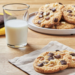 Un verre de lait et une assiette de biscuits aux pépites de chocolat sont disposés sur une table en bois, suggérant une collation réconfortante.