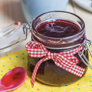Un pot de confiture maison est dACcorAC d'un ruban A? carreaux rouge et blanc, posAC sur une surface A? pois avec une cuillA?re de confiture A? proximitAC.