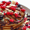 Une pile de crAapes arrosACes de sirop de chocolat et garnies de baies et d'amandes effilACes.