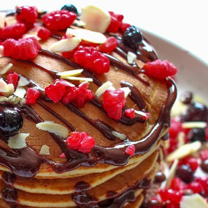 Une pile de crAapes arrosACes de sirop de chocolat et garnies de baies et d'amandes effilACes.