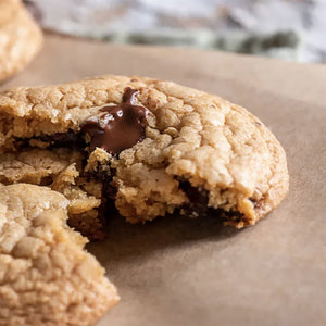 Gros plan d'un biscuit aux pACpites de chocolat partiellement mangAC sur du papier sulfurisAC, mettant en ACvidence sa texture et le chocolat fondu.