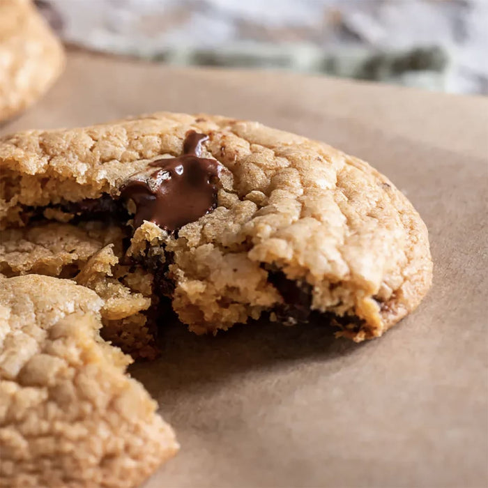 Gros plan d'un biscuit aux pACpites de chocolat partiellement mangAC sur du papier sulfurisAC, mettant en ACvidence sa texture et le chocolat fondu.