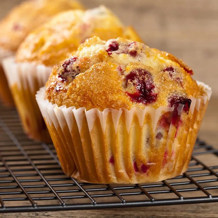 Une rangACe de muffins aux canneberges fraARchement cuits dans des moules en papier repose sur une grille.