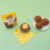 Un paquet de mAClange A? muffins Krusteaz 3-en-1 est prACsentAC A? cA?tAC de muffins au chocolat dACcorACs et simples sur une surface vert clair avec des confettis.