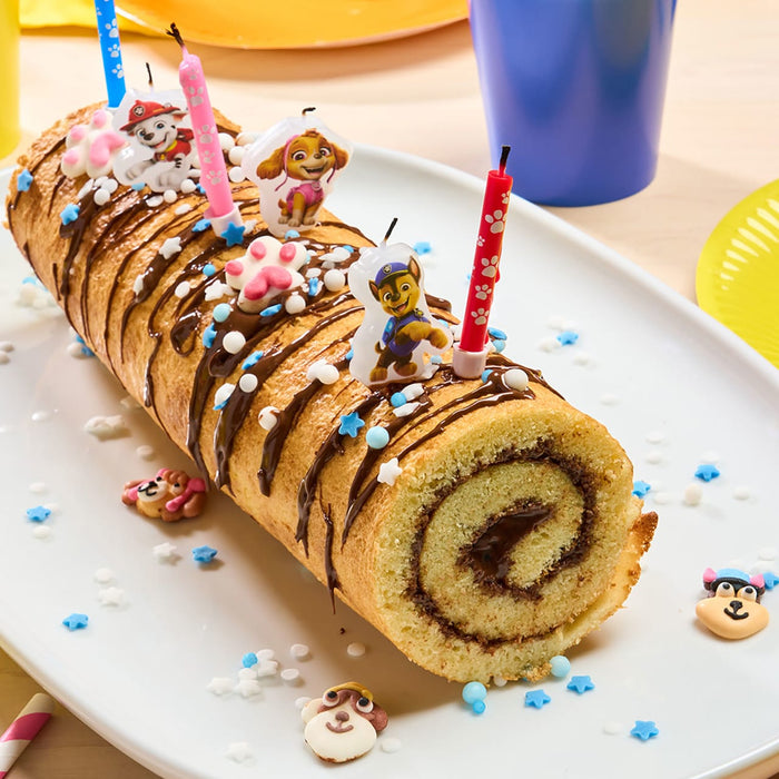 Un gActeau roulAC festif dACcorAC de filets de chocolat, de vermicelles, de bougies et de dACcorations sur le thA?me de Paw Patrol, probablement pour une fAate d'anniversaire.
