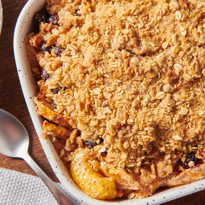 Un gros plan en plongée d'un crumble aux fruits fraîchement cuit, réalisé dans le cadre des Vahine Hero Recipes, avec une garniture dorée à l'avoine dans un plat blanc moucheté.