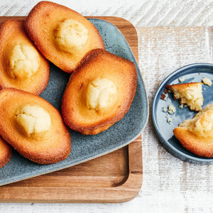 Des madeleines dorées sont artistiquement disposées sur une assiette bleue, présentant une délicieuse recette de la collection Vahine Nutritional Ingredients And Hero Recipe Images.