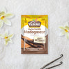 Un sachet de sucre vanillAC VahinAC Madagascar est prACsentAC sur un fond de gousses de vanille et de fleurs, soulignant sa saveur intense.