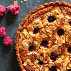 Une délicieuse tarte aux amandes et aux framboises avec une croûte dorée et des amandes grillées.