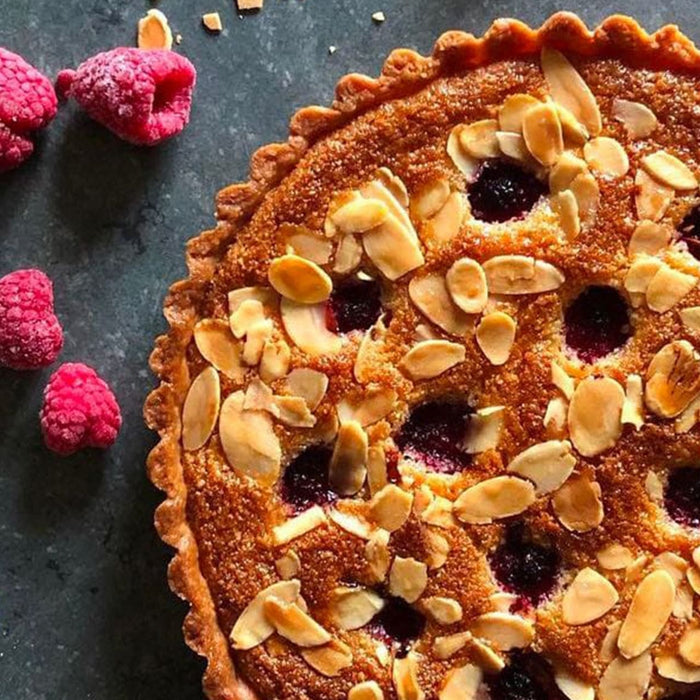 Une délicieuse tarte aux amandes et aux framboises avec une croûte dorée et des amandes grillées.